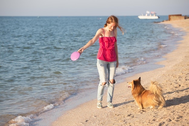 Fröhliches Spaßwochenende am Meer - Mädchen, das mit einem Hund am Strand am Frisbee spielt. Sommer