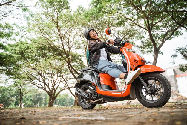 Foto fröhliches studentenmädchen mit helm und jacke fährt mit dem motorrad zur schule