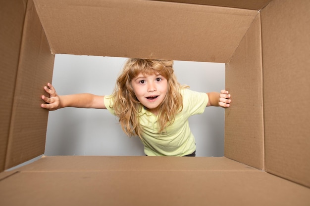 Fröhliches süßes Kind, das ein Geschenk öffnet Kartons Pakete Lieferservice-Konzept Kinderausdruck überraschtes Gesicht