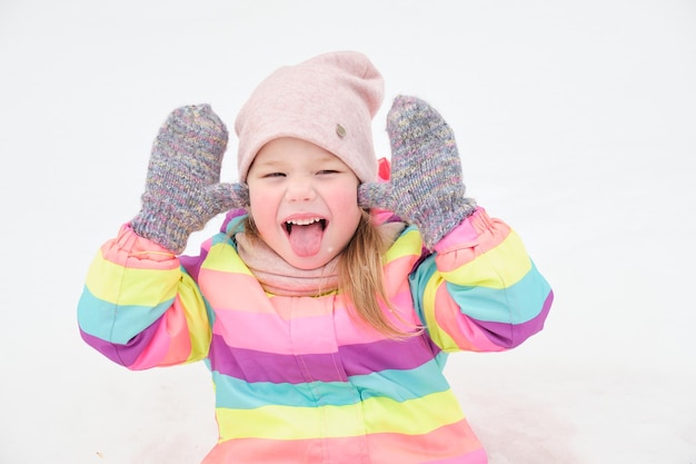 Fröhliches süßes Mädchen im Alter von 5 Jahren spielt im Schnee und macht lustige Gesichter