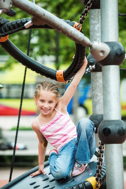 Fröhliches, süßes und lächelndes kleines Mädchen, das draußen auf dem Spielplatz spielt