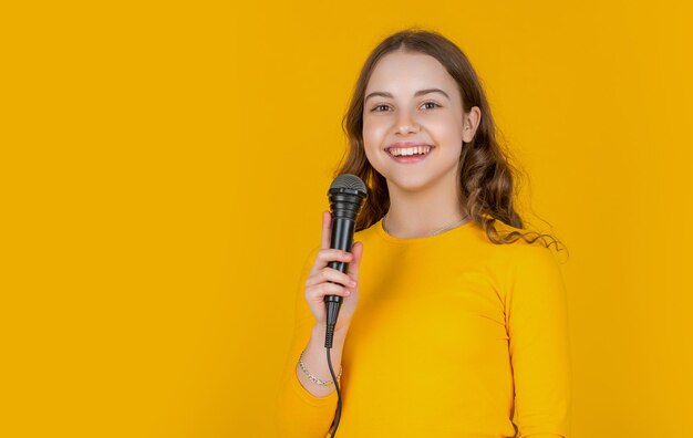 Foto fröhliches teenager-kind mit mikrofon auf gelbem hintergrund