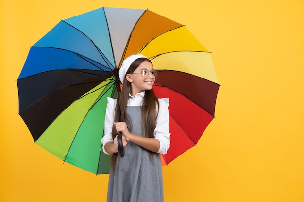 Fröhliches Teenager-Kind unter buntem Sonnenschirm Kind in Baskenmütze mit Regenschirm Herbstsaison Regenwettervorhersage zurück zur Schule Tween mit lebendigem Regenschutz glückliches Schulmädchen mit Brille