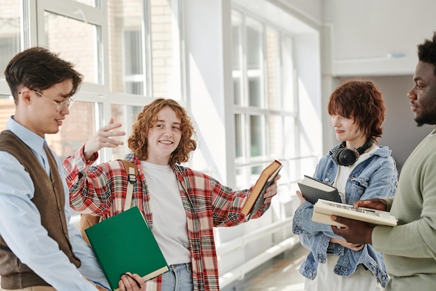 Foto fröhliches teenager-mädchen, das ihren interkulturellen klassenkameraden den plot des buches erklärt