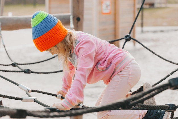 Fröhliches Teenager-Mädchen, das im Seilspinnennetz am Spielplatz spielt. Kindersport.