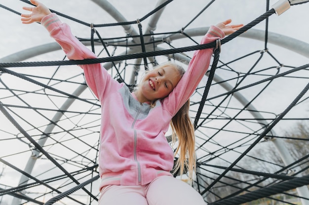 Fröhliches Teenager-Mädchen, das im Seilspinnennetz am Spielplatz spielt. Kindersport.