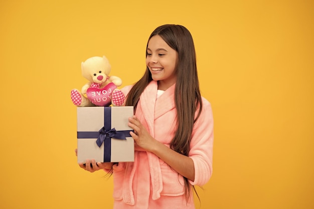 Fröhliches Teenager-Mädchen im Frottee-Bademantel mit Spielzeug und Geschenkbox zum Geburtstag