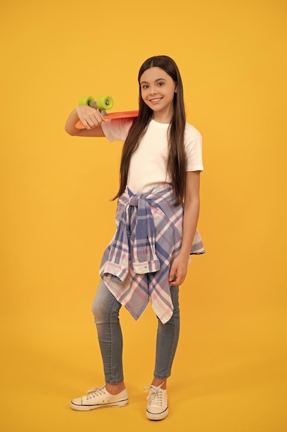 Fröhliches Teenager-Mädchen im Teenie-Casual-Holding-Skater-Mädchen mit Pennyboard auf gelbem Hintergrund
