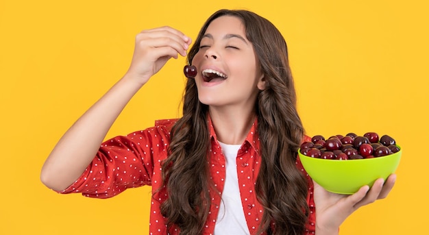 Fröhliches Teenager-Mädchen isst Kirschschale auf gelbem Hintergrund