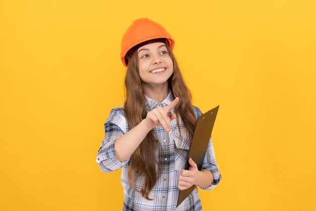 Fröhliches Teenager-Mädchen mit Helm und kariertem Hemd, das sich Notizen in der Zwischenablage macht