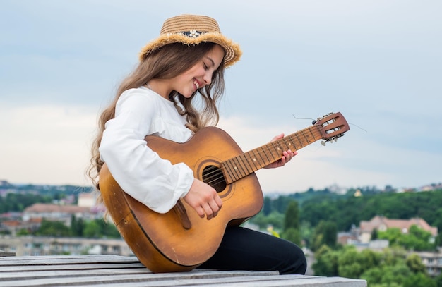 Fröhliches Teenager-Mädchen spielt Akustikgitarre im Freien auf Himmelshintergrundmusik