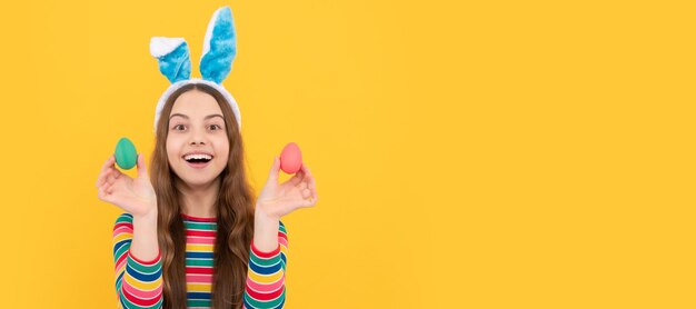 Fröhliches Teenie-Mädchen zu Ostern in Hasenohren, das bemalte Eier für die Eiersuche im Urlaub hält