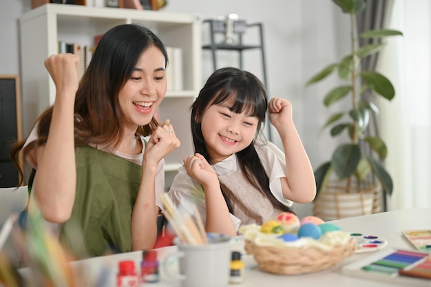 Fröhliches und aufgeregtes kleines asiatisches Mädchen malt gerne Ostereier mit ihrer Mutter