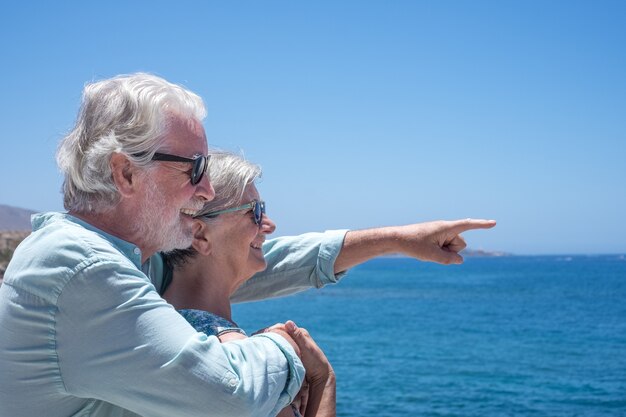 Fröhliches und entspanntes Seniorenpaar vor dem Meer mit Blick auf den Horizont über dem Wasser. Zwei Rentner genießen Sommer und Urlaub