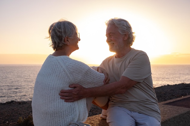 Fröhliches und romantisches kaukasisches Paar umarmte sich am Meer bei Sonnenuntergang und blickte in die Augen Altes Ehepaar im Freien, das gemeinsam Urlaub macht