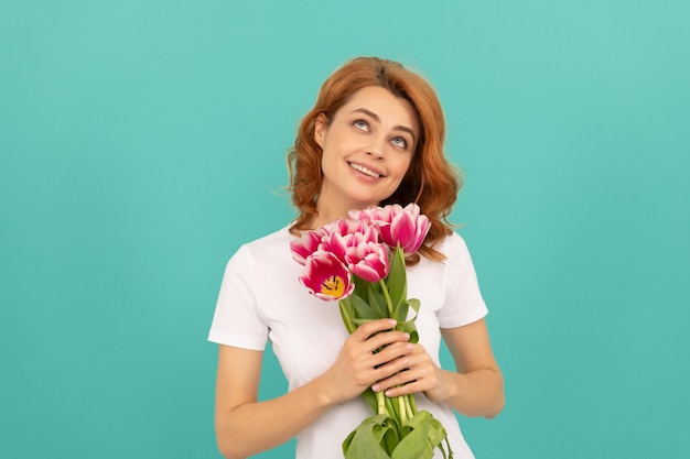 Fröhliches verträumtes Mädchen mit Tulpenblumenstrauß auf blauem Hintergrund