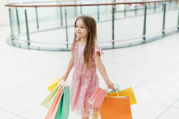 Fröhliches Vorschulmädchen, das mit Einkaufstüten geht. Hübsches lächelndes kleines Mädchen mit Einkaufstüten, die im Geschäft aufwerfen. Das Konzept des Einkaufens in Geschäften