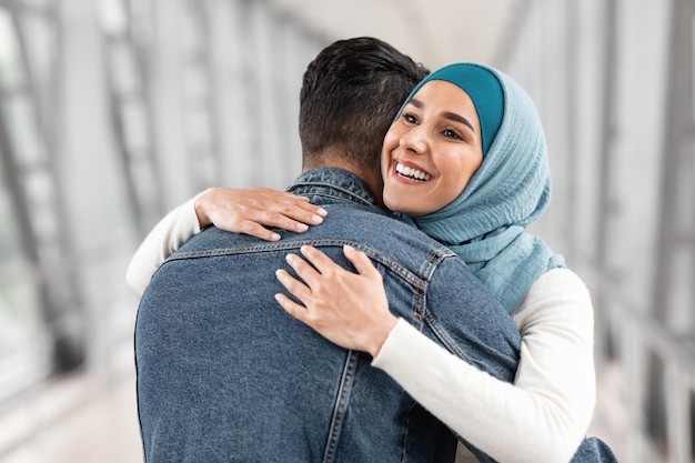 Fröhliches Wiedersehen fröhliche muslimische Frau im Hijab, die ihren Mann am Flughafen umarmt