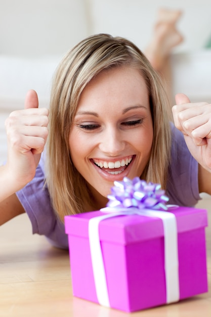 Frohe Frau, die ein Geschenk liegt auf dem Boden betrachtet