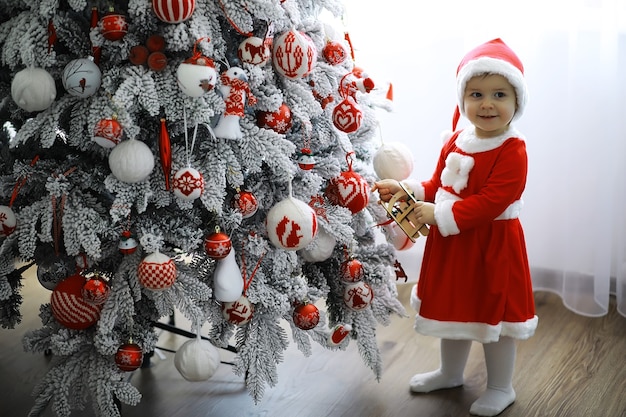 Frohe helle Weihnachten. Schönes Baby, genießen Sie Weihnachten. Kindheitserinnerungen. Kleines Kind des Sankt-Mädchens feiert Weihnachten zu Hause. Familienurlaub. Nettes Kind fröhliches Stimmungsspiel des Mädchens nahe Weihnachtsbaum.