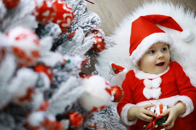 Frohe helle Weihnachten. Schönes Baby, genießen Sie Weihnachten. Kindheitserinnerungen. Kleines Kind des Sankt-Mädchens feiert Weihnachten zu Hause. Familienurlaub. Nettes Kind fröhliches Stimmungsspiel des Mädchens nahe Weihnachtsbaum.