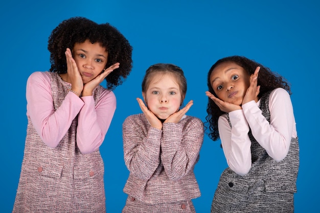 Frohe internationale kleine Freundinnen in lässigen Puffbacken haben gemeinsam Spaß isoliert auf Blau