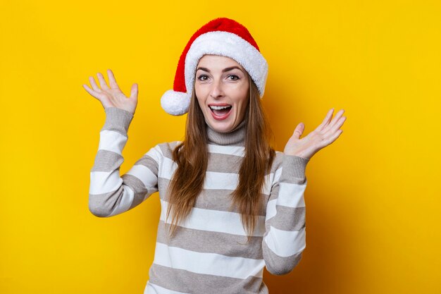 Frohe junge Frau im Weihnachtsmann-Hut auf gelbem Grund.