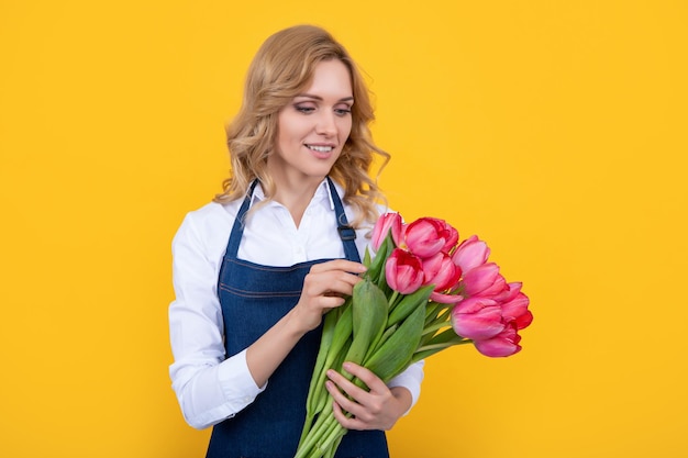 Frohe junge Frau in Schürze mit Frühlingstulpenblumen auf gelbem Hintergrund