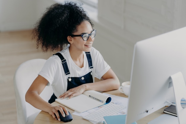 Frohe junge Frau sitzt vor modernem Computer