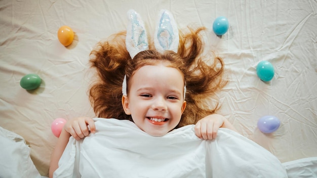 Frohe Ostern Ein süßes und lustiges kleines Mädchen genießt Ostereier mit Hasenohren und liegt im Bett