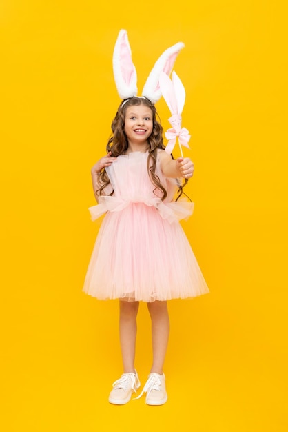 Frohe Ostern für Kinder Ein lockiges Mädchen, gekleidet in einen Osterhasen Ein außergewöhnlich schönes Teenager-Mädchen mit langen Ohren und einem üppigen Kleid auf gelbem, isoliertem Hintergrund