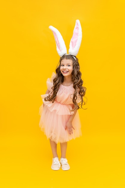 Frohe Ostern für Kinder Ein lockiges Mädchen, gekleidet in einen Osterhasen Ein außergewöhnlich schönes Teenager-Mädchen mit langen Ohren und einem üppigen Kleid auf gelbem, isoliertem Hintergrund