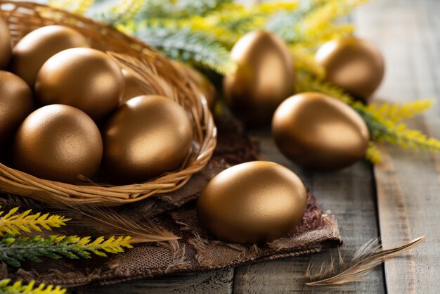 Frohe Ostern! Golden von Ostereiern im Nest und von der Feder auf hölzernem Hintergrund