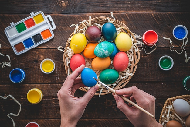 Frohe Ostern. Malen und Vorbereiten von bunten Eiern für Osterferien. Draufsicht. Farbige Eier in einem Korb auf einem Holztisch, flach liegen