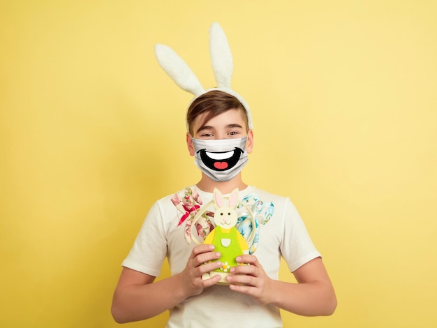 Frohe Ostern. Porträt eines jungen kaukasischen Jungen mit Emotionen auf seiner schützenden Gesichtsmaske isoliert auf Studiohintergrund. Schönes männliches Model. Menschliche Emotionen, Gesichtsausdruck, Verkauf, Anzeigenkonzept.