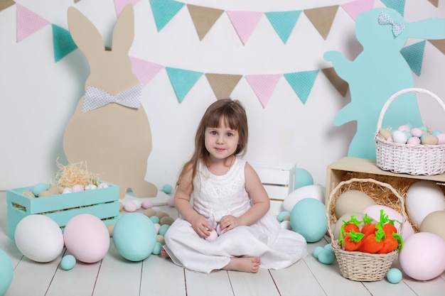 Frohe Ostern!! Schönes kleines Mädchen in einem weißen Kleid mit Ostereiern und einem Korb auf einer hellen Ostern-Landschaft. Hase und Korb. Große Ostereier, bunter Standort. Muttertag. Ernte, Bauer