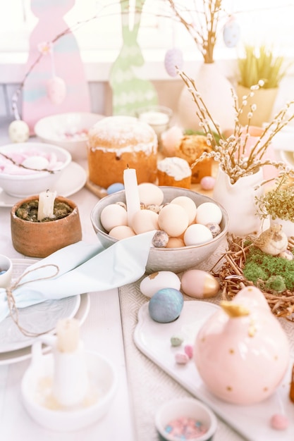 Frohe ostern und frühlingsferien zeit festliche tischlandschaft set dekor traditionelles abendessen essen ostereier und gebackene kuchen auf dem tisch zu hause kaninchen und weide blasser pop pastellblau und rosa farbaufflackern