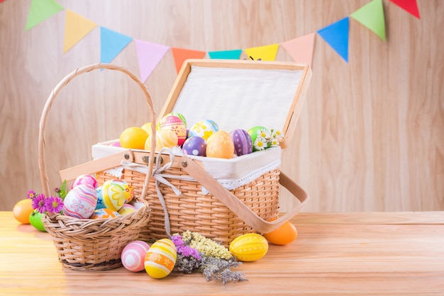 Frohe Ostertag bunte Eier und Blumen im Korb auf Holzboden haben verschwommen feiern Partyflaggen