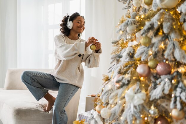 Frohe Weihnachten afrikanisch-amerikanische Frau mit Kopfhörern, die Musik hört und den Weihnachtsbaum schmückt