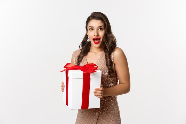 Frohe Weihnachten. Bild einer schönen Frau in einem glamourösen Kleid, die ein Geschenk erhält und überrascht aussieht, das neue Jahr feiert und auf weißem Hintergrund steht