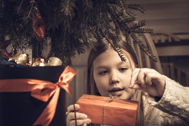 Frohe Weihnachten frohe Feiertage Fröhliches süßes kleines blondes Mädchen öffnet ein Weihnachtsgeschenk