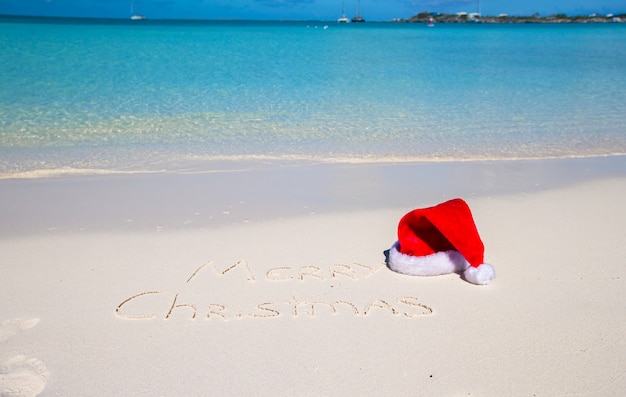 Frohe weihnachten geschrieben auf weißen sand des tropischen strandes mit weihnachtshut