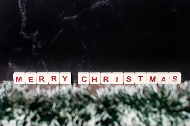 Frohe Weihnachten, geschrieben mit Buchstaben aus einem Spiel und Weihnachtsschmuck auf dunklem Hintergrund