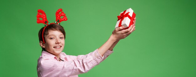 Frohe weihnachten glücklicher teenager mit rotem geweih mit einem geschenk in den händen auf grünem hintergrund kaukasier...