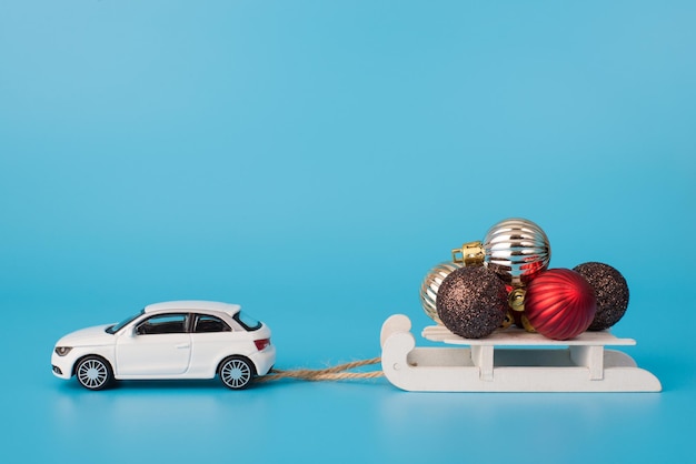 Frohe Weihnachten-Konzept. Foto eines modernen Autos mit seitlicher Ansicht, das Schlitten mit einem Sprung von verschiedenen bunten Baumdekoren einzeln auf blauem Hintergrund trägt