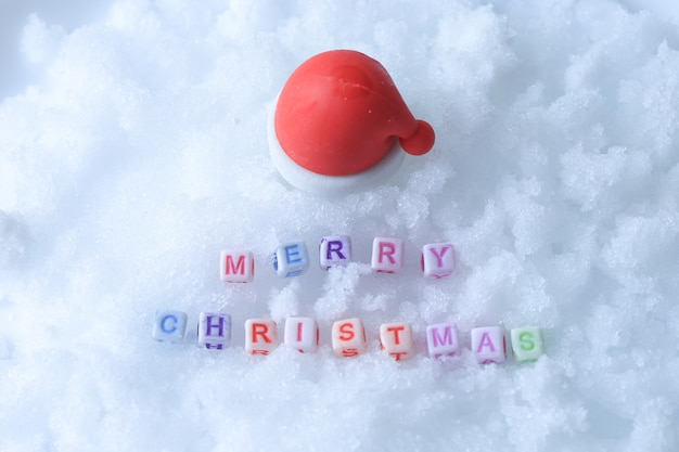 Frohe Weihnachten Nachricht gemacht mit Buchstabenwürfeln über Schnee und Weihnachtsmütze