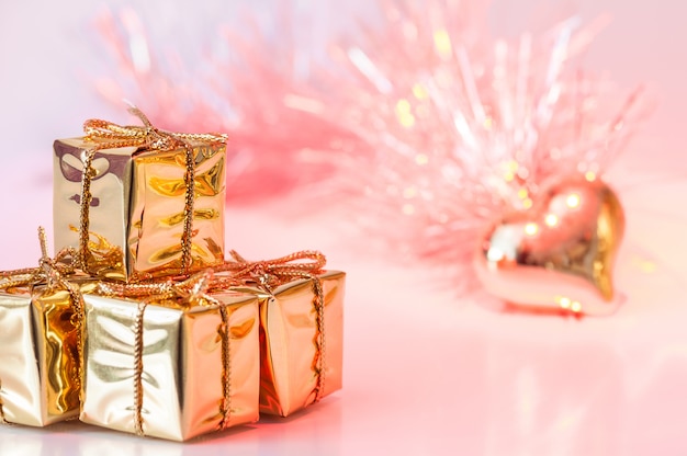 Frohe weihnachten, neues jahr, geschenke in den goldkästen und ein goldenes herz auf einem hintergrund des rosa und gelben bokeh.