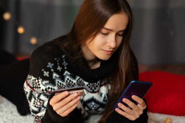 Frohe Weihnachten und ein glückliches Neues Jahr. Mädchen macht Online-Shopping auf dem Smartphone