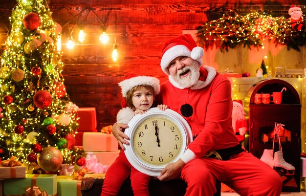 Foto frohe weihnachten und frohes neujahr weihnachtsmann und kleine weihnachte assistent mit alter uhr zeit zu