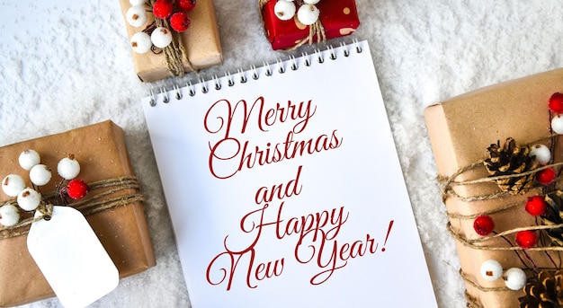 FROHE WEIHNACHTEN UND HAPPY NEW YEAR Text Zero Waste Weihnachtstext mit Geschenken mit Dekorationen auf weißem Schneehintergrund. Umweltfreundlich verpacktes Geschenk mit Anhängern aus Bastelkarton.